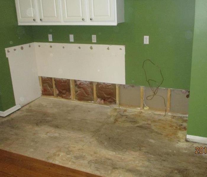 A green kitchen with white cabinets and medium brown color luxury vinyl flooring that suffered water damage .
